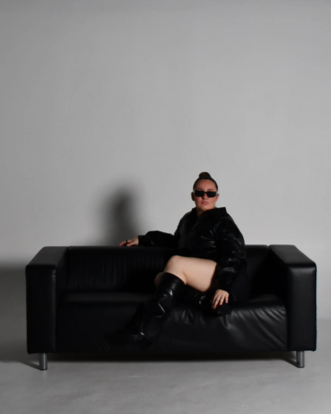 Sabrina on a black leather sofa in sunglasses and knee-high boots