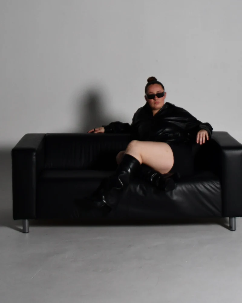 Sabrina leaning back on a black leather sofa